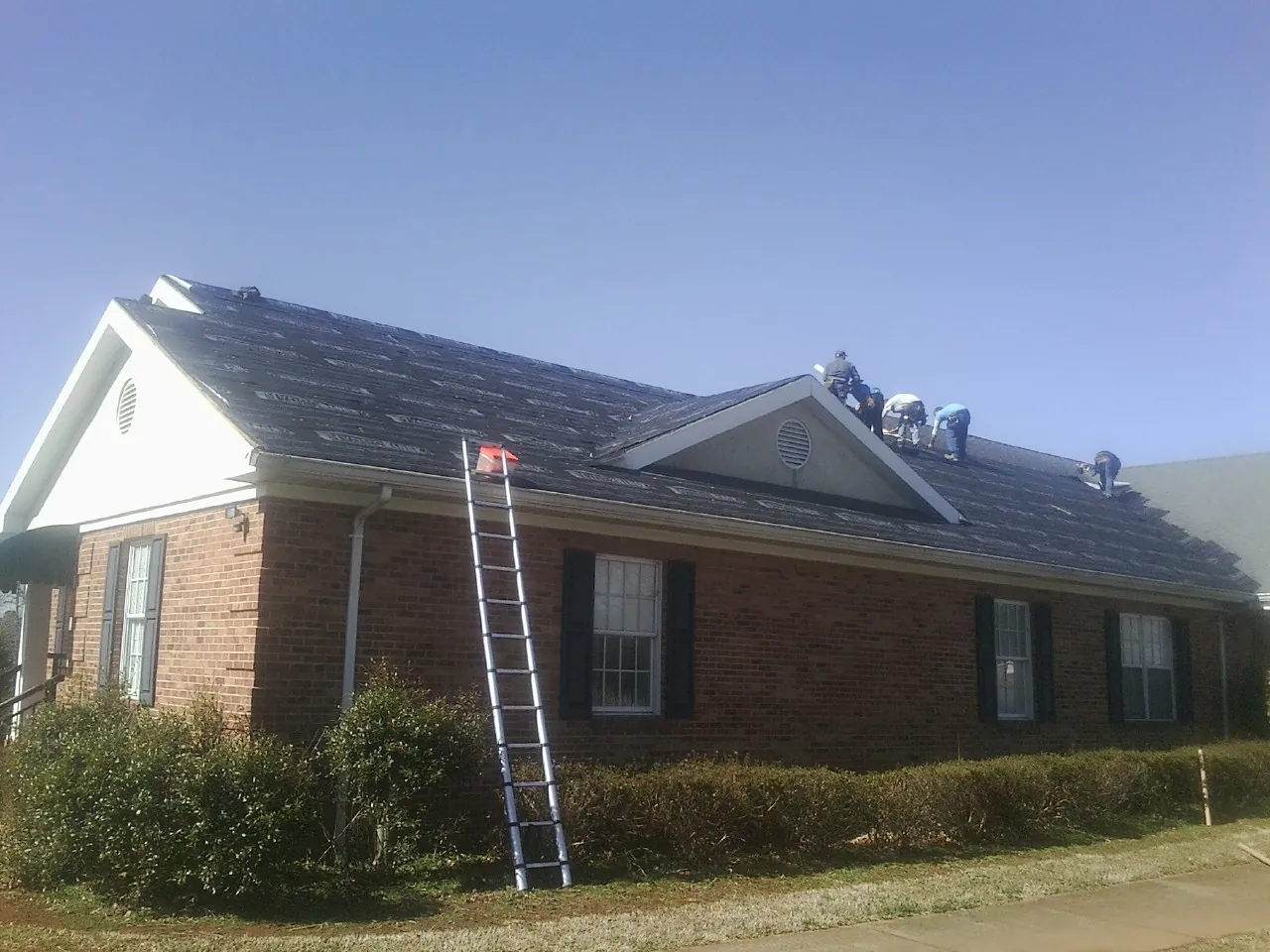 Crew tearing shingles off a brick ranch roof with a ladder set — Emergency Roof Repair work by our crew in Stevensville
