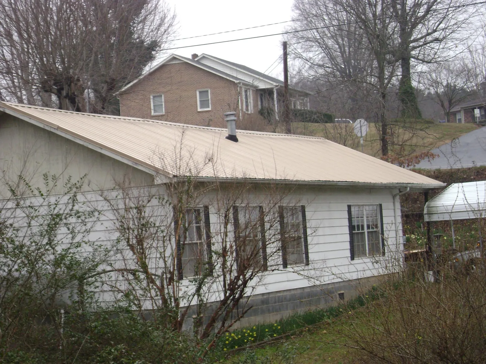 Tan metal roof on a white sided house set into a hillside — Commercial Roofing by Roofing Brothers in Stevensville